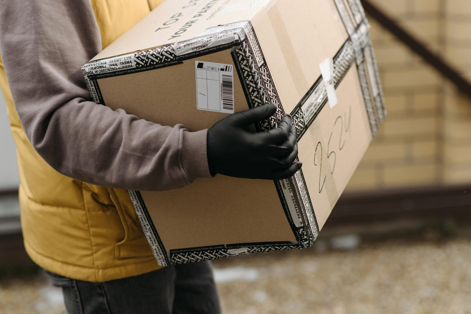 Courier holding a package marked 'TOP PACKAGING' wearing gloves for safe delivery.